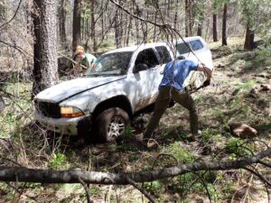 Two monitoring staff dig out a vehicle stuck in the mud off a dirt road.